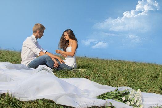 Young couple sitting on summer field discussing something and smiling