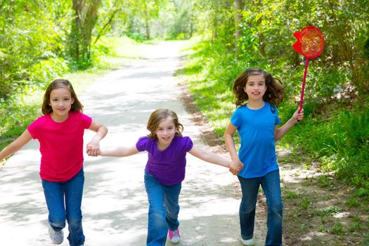 Friends and sister girls running in the forest track smiling happy with butterfly net