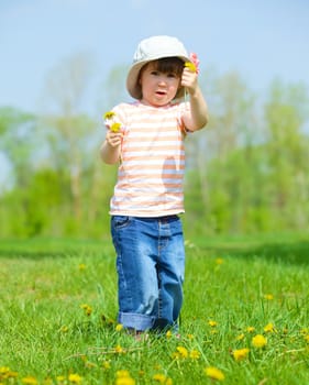 Sweet beautiful girl sitting on a green meadow with dandelions