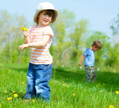 Sweet beautiful girl sitting on a green meadow with dandelions