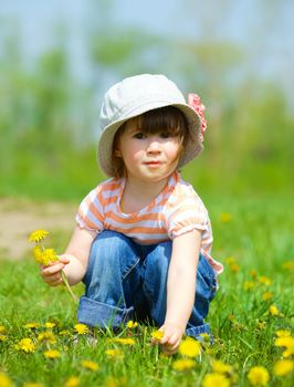 Sweet beautiful girl sitting on a green meadow with dandelions