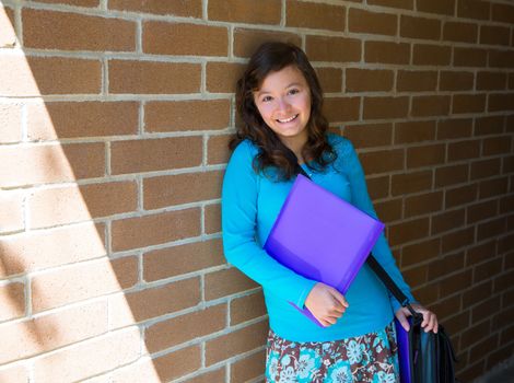 Schoolgirl teenager at school brick wall happy with folder and bag