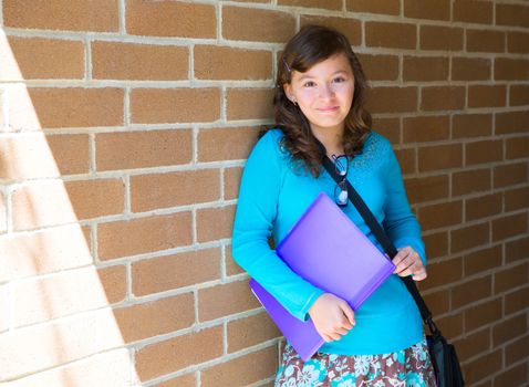 Schoolgirl teenager at school brick wall happy with folder and bag