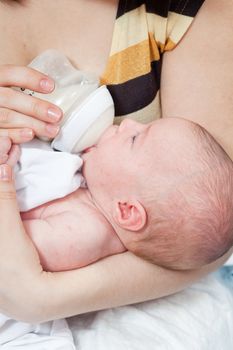 Mother feeds the chest baby from a children's small bottle