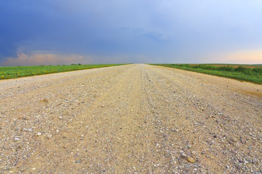 Dirt road through the field and approaching storm