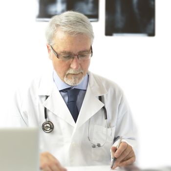 Doctor with scrubs and stethoscope writing a prescription, on the white background with x-rays.