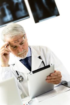 Doctor in clinic sitting at desk looking at x-rays on tablet, white background with x-rays.