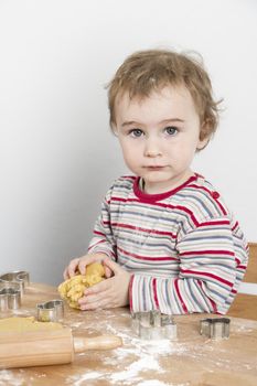 vertical image of 2 year old child making biscuit  at wooden desk