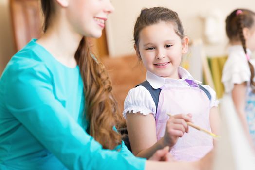 girl interested in drawing the teacher in the background paint other children