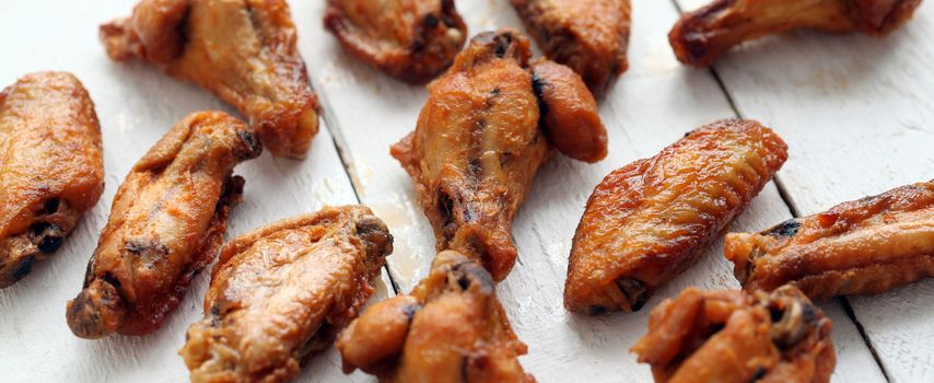 Grilled tasty chicken wings on a white wooden table