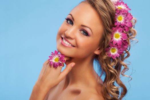 Beautiful young caucasian woman with flowers in her hair over blue background