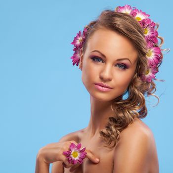 Beautiful young caucasian woman with flowers in her hair over blue background