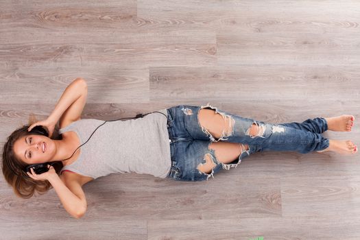 Beautiful caucasian woman listening music with headphones lying on the wooden floor