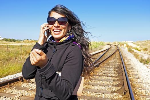 Young beautiful woman is phoning at a railroad track