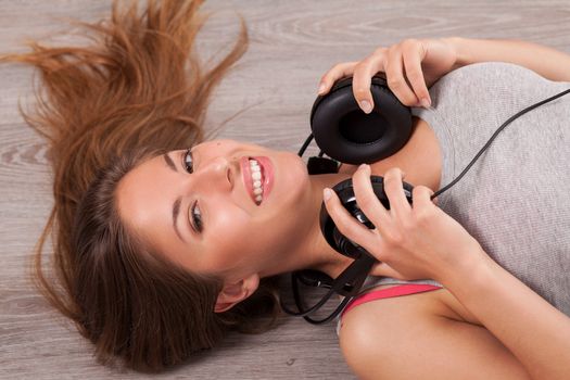 Beautiful caucasian woman listening music with headphones lying on the wooden floor