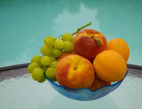 Peaches, grape and apricots in glass plate on table by the swimming pool