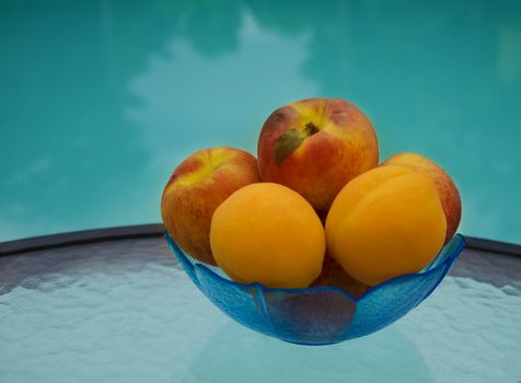Peaches and apricots in glass plate on table by the swimming pool