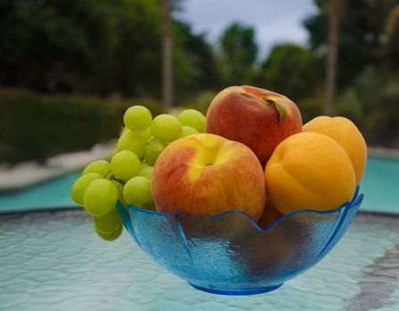 Grape, peaches and apricots in glass plate on table by the swimming pool