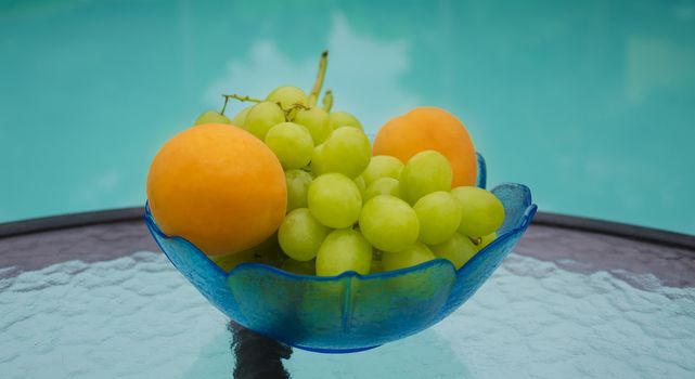 Grape and apricots in glass plate on table by the swimming pool