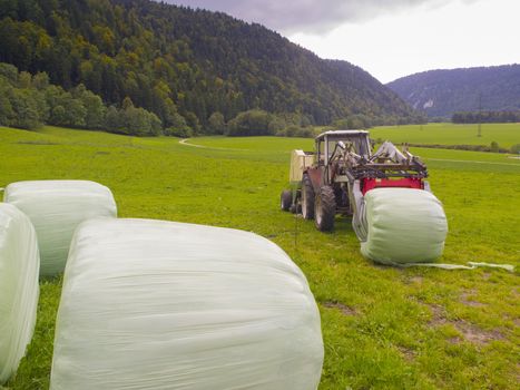 Farm Tractor gathering Hay Bales before winter in Switzerland