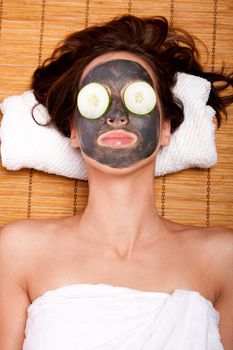 Woman face with beauty treatment skincare mask and cucumber laying on bamboo at spa.