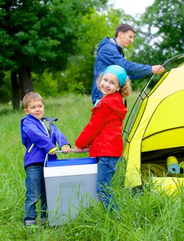 Summer, family camping - lovely sister and brother have a refrigerator with father near camp tent. Vertical view