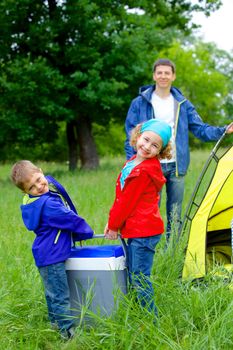 Summer, family camping - lovely sister and brother have a refrigerator with father near camp tent. Vertical view