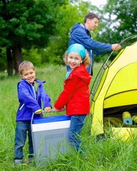 Summer, family camping - lovely sister and brother have a refrigerator with father near camp tent. Vertical view