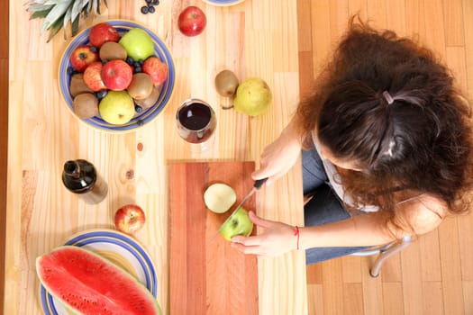 A young adult woman cutting fruits in the kitchen.