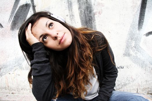 A young woman listening to melancholic Music and sitting on the pavement.