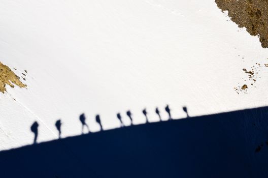 Shadows of group of mountain trekkers walking on a snow