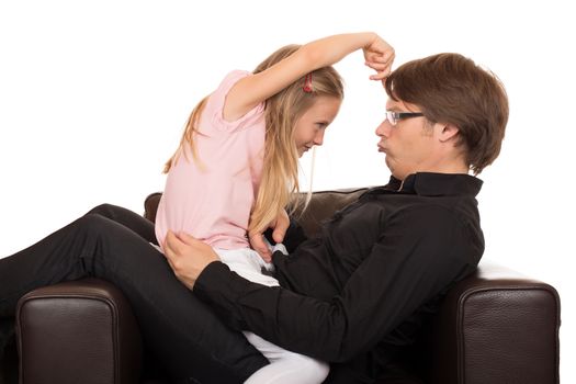 Young father play and make grimace to his daughter and she pointing her finger on his forehead in a brown leather armchair. Isolated on white background.