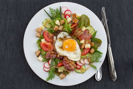 Greek salad also called peasant salad, village salad or country salad. Composed with lettuce, cucumber, onion, radish, fried egg and bacon, cheese, tomatoes, parsley and croutons.