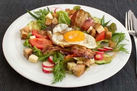 Village salad also called peasant salad, greek salad or country salad. Composed with lettuce, cucumber, onion, radish, fried egg and bacon, cheese, tomatoes, parsley and croutons.