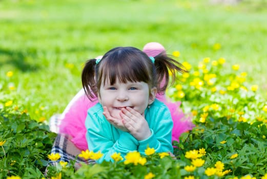 little girl lies on a glade with dandelions and smiles