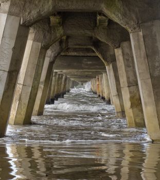Ocean surf and concrete foundation pilings of longest pier Tolaga Bay Wharf in Gisborne North Island New Zealand