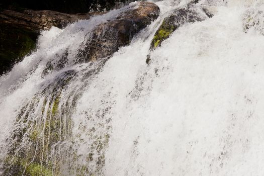 Curtain of clear clean water cascading down high rocky cliff creating a refreshing cool waterfall