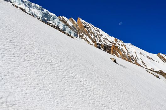 Snow mountains slope with rocks, with glacier and blue sky with moon