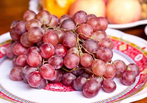 Red grape berries in white plate on straw tray closeup
