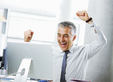 Happy mature businessman in office arms raised. 