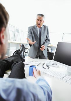 Business man relaxing at desk while his boss shouting angry