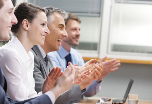 Group of cheerful businesspeople sitting in a row on a presentation and clapping