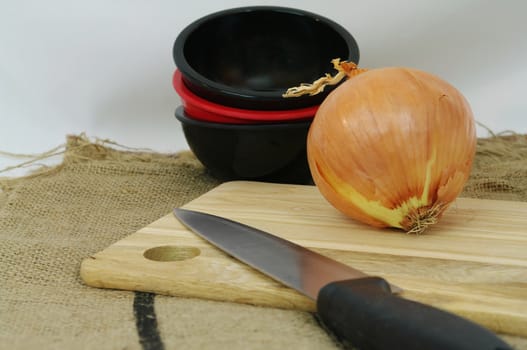 Onion uncut on a bamboo board beside stacked red and black bowls