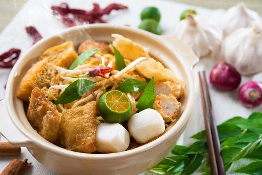 Hot and spicy Singapore Curry Noodle or laksa  mee with hot steam in clay pot, decoration setup, serve with chopsticks. Singaporean cuisine.