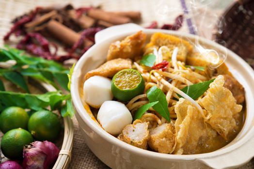 Hot and spicy Malaysia Curry Noodle or laksa  mee with hot steam in clay pot, decoration setup, serve with chopsticks. Malaysian cuisine.