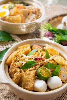 Hot and spicy Malaysian Curry Noodles or laksa  mee with hot steam in clay pot, decoration setup, serve with chopsticks. Malaysia cuisine.