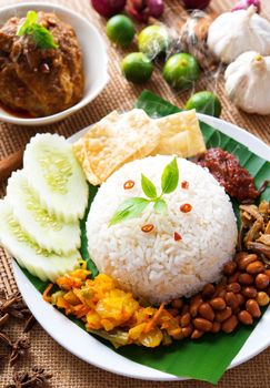 Nasi lemak traditional malaysian spicy rice dish, fresh cooked with hot steam. Served with belacan, ikan bilis, acar, peanuts and cucumber. Decoration setup.