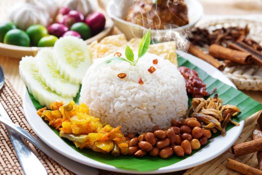 Nasi lemak traditional malaysian hot and spicy rice dish, fresh cooked with hot steam. Served with belacan, ikan bilis, acar, peanuts and cucumber. Decoration setup.