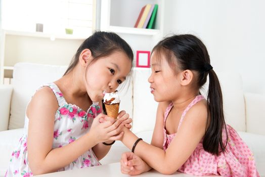 Eating ice cream. Asian girls sharing an ice cream. Beautiful children model at home.