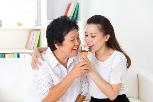 Sharing food. Happy Asian family sharing an ice cream at home. Beautiful senior mother and adult daughter eating dessert together. 